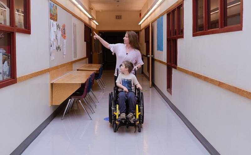 Education Assistant with student in wheelchair in hallway
