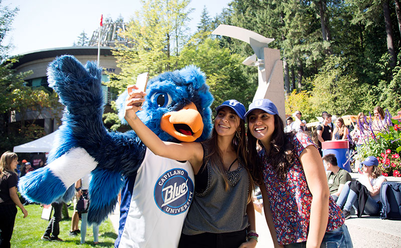 Two students taking a photo with the CapU mascot, Jay