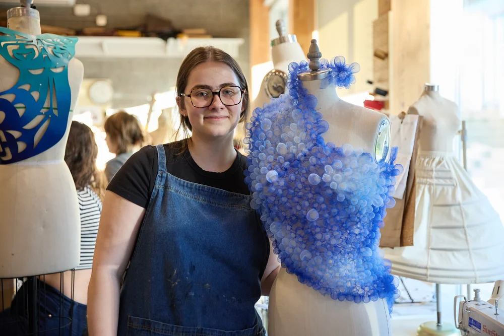 A costuming student beside a garment on a dress form in the CapU studio