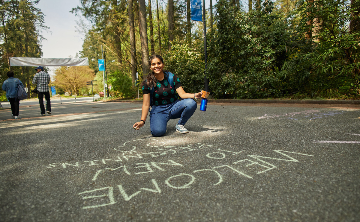 Student writing a welcome on the ground in chalk for summer orientation