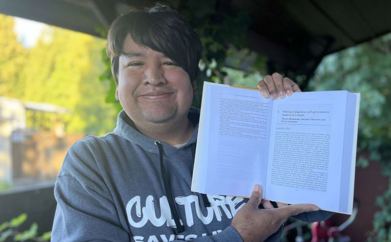 Mason Ducharme proudly holds his first academic publication, where he was the lead author of a chapter titled 