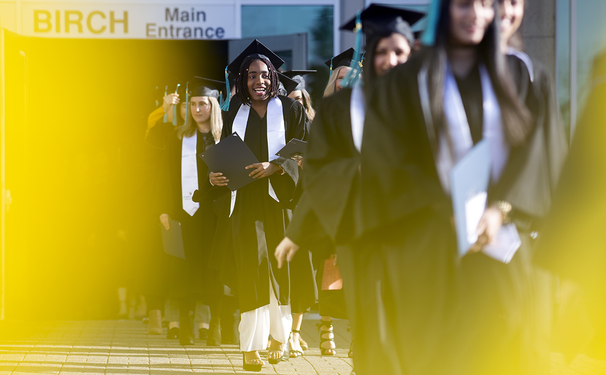 students smiling and walking in graduation robes and caps