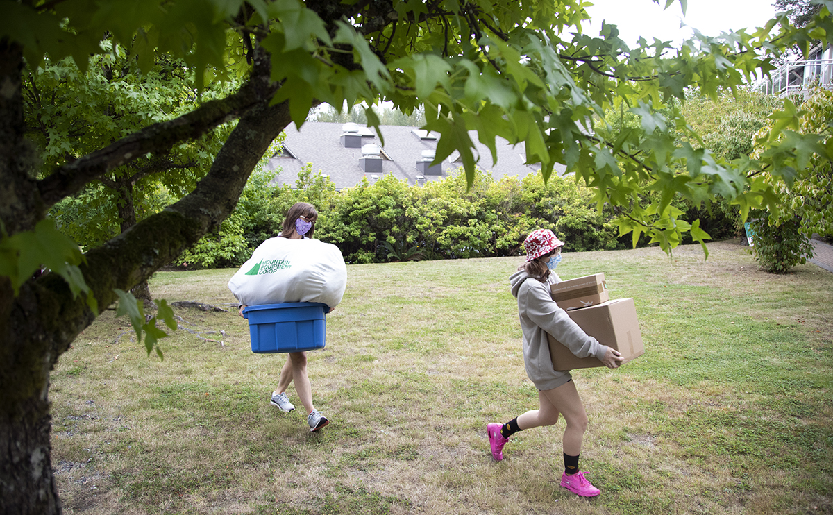 A mom and daughter, wearing masks, carrying boxes