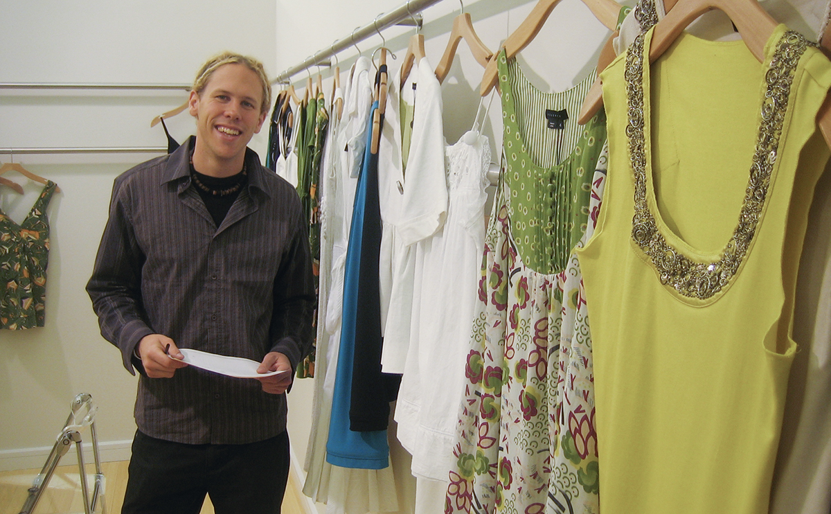 Sean Aiken working as a fashion designer, posing next to rack of clothes