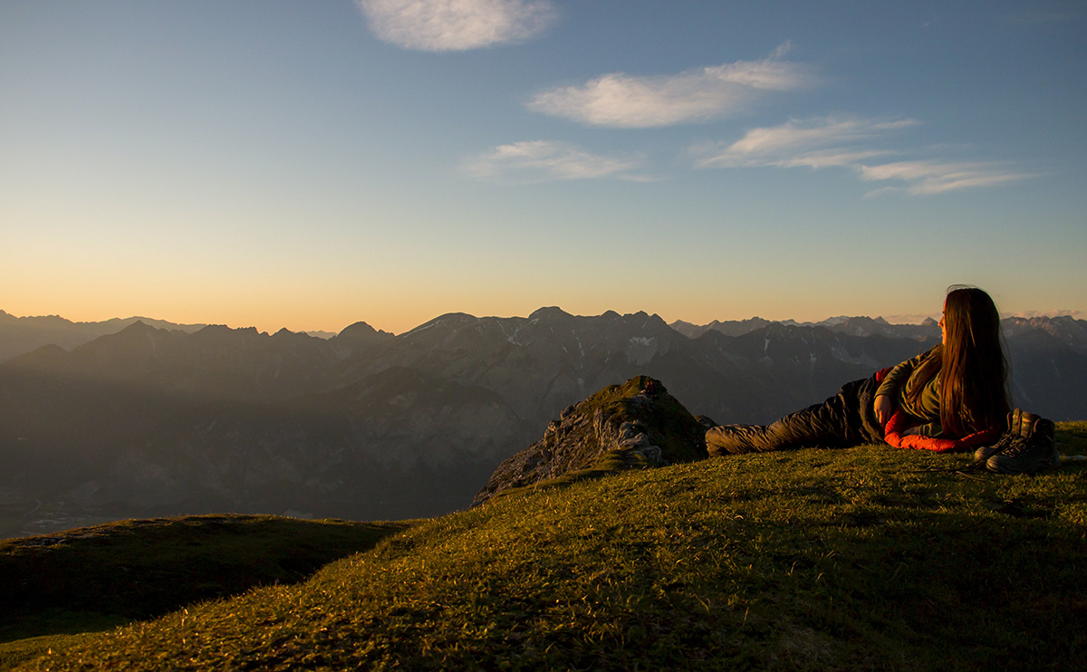 Student lying in sleeping bag looking at mountains during sunset