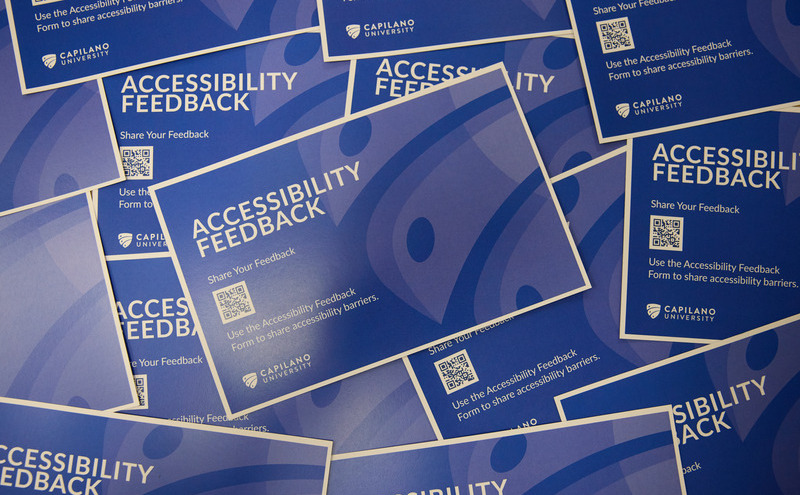 A flat lay of blue Capilano University accessibility feedback posters featuring qR codes for sharing barrier feedback.
