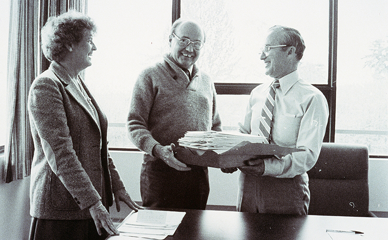 Outgoing president, Paul Gallagher, hands documents over to new president, Doug Jardine, while Board Chair, Hilda Rizun, looks on.