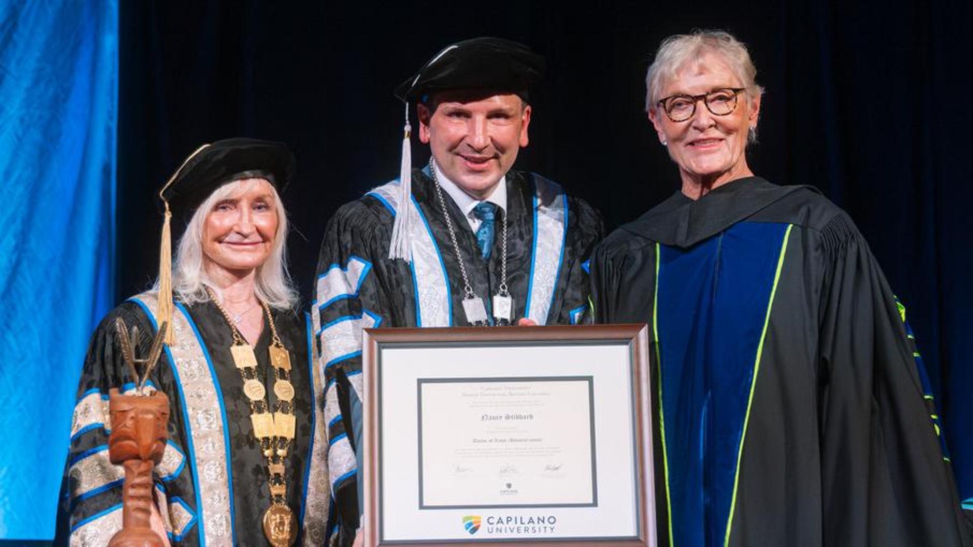 Capilano University Chancellor Debra Doucette and President Jason Dewling present a 2026 Honorary Degree award to Nancy Stibbard on stage.