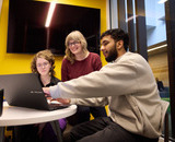 Writing & Literature instructor Dara Greaves working with two students at a laptop.
