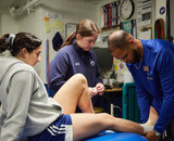 Kinesiology students wrapping an athlete's ankle with tape.
