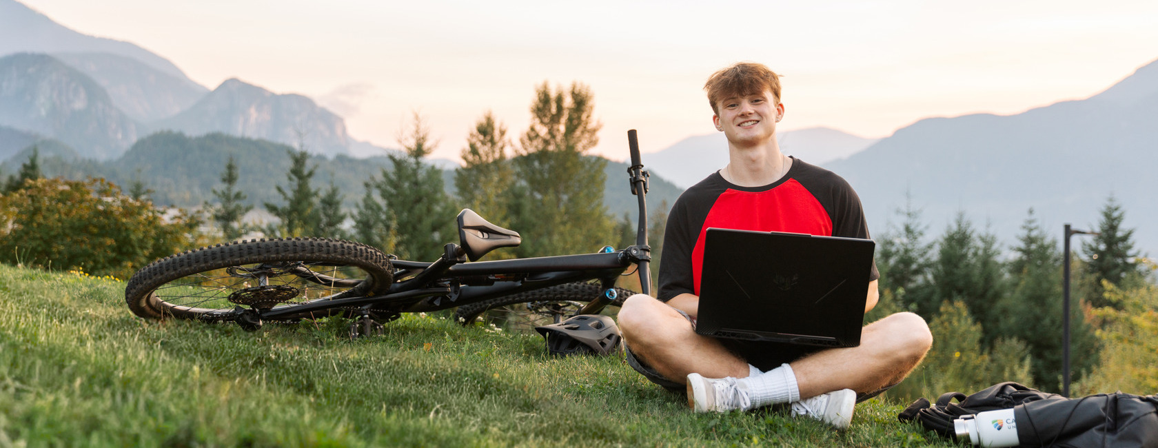 CapU student Jasper studying at CapU Squamish, seated with a laptop in his lap and a bike on his right.