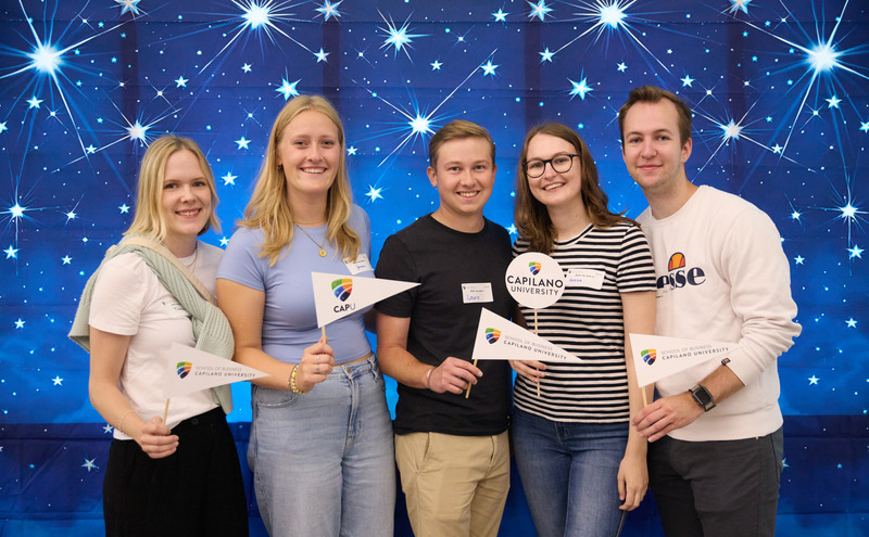 Five CapU students at the School of Business Orientation holding little flags.