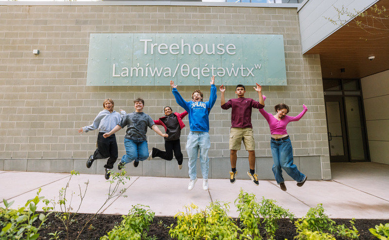 students jumping in front of Treehouse sign