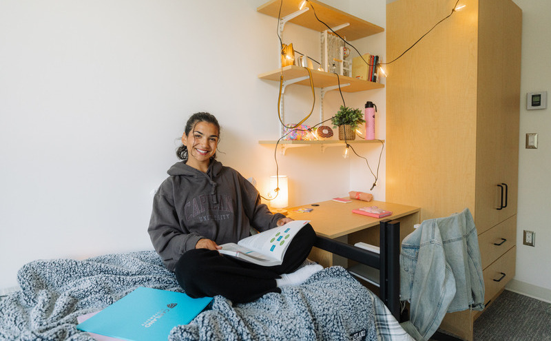 A student sitting on their dorm bed smiling