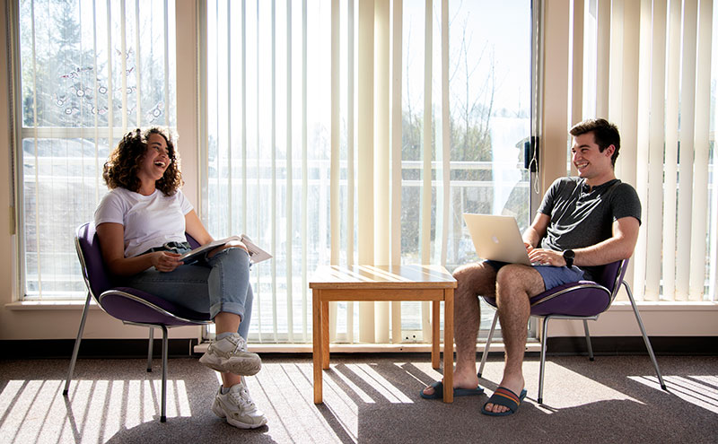 Students sitting in chairs talking in CapU Residence common area