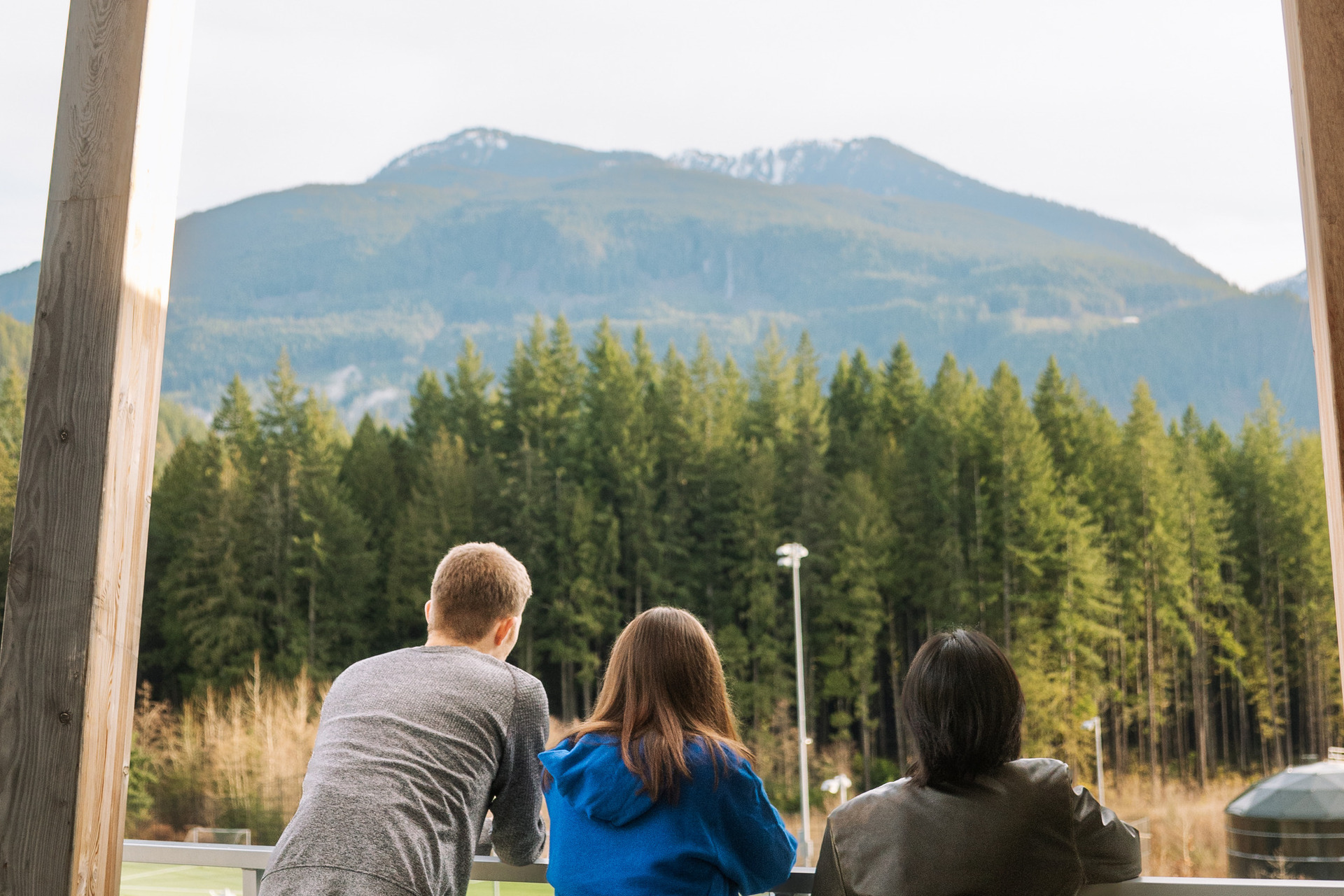 Three students looking out at the forest and mountains of Squamish, B.C. at the CapU Squamish Campus housing.